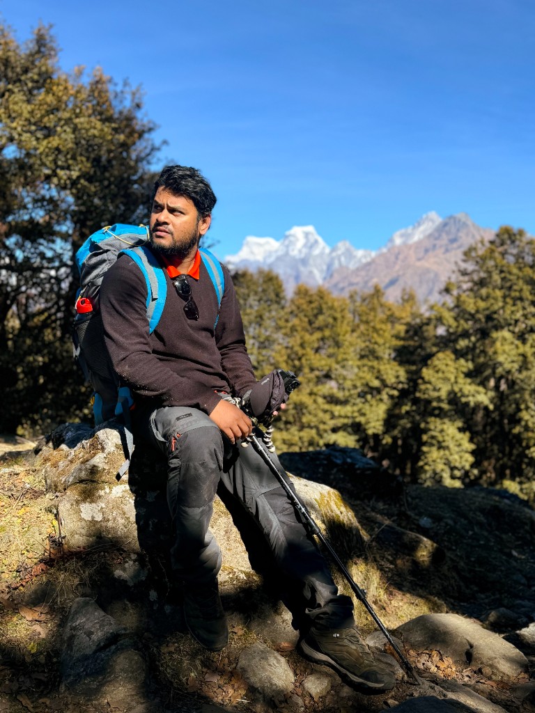 Trekker resting on a rock with snow-capped Himalayan peaks in the distance.